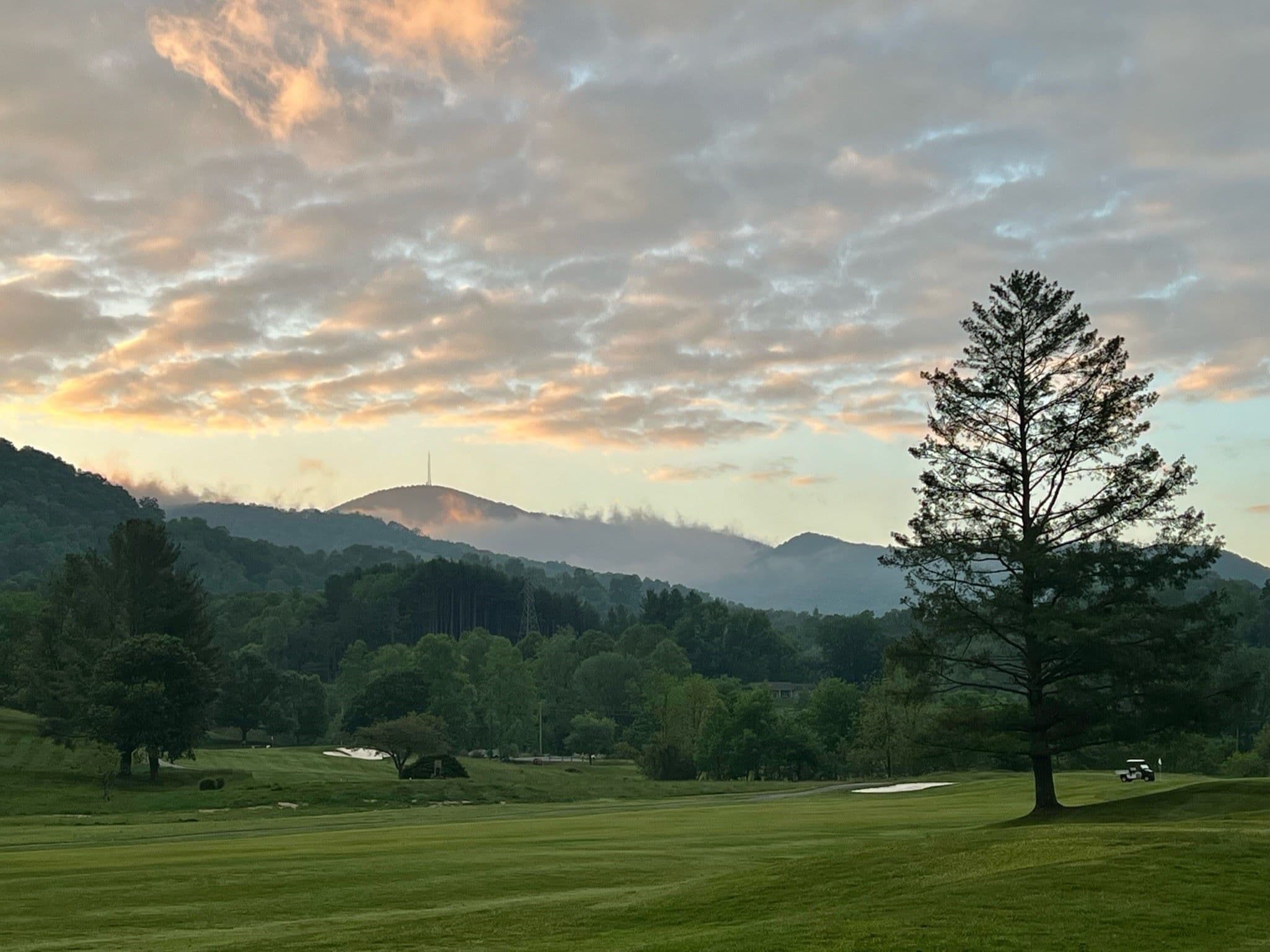 A serene landscape featuring a tree with mountains and clouds at sunrise in the background.