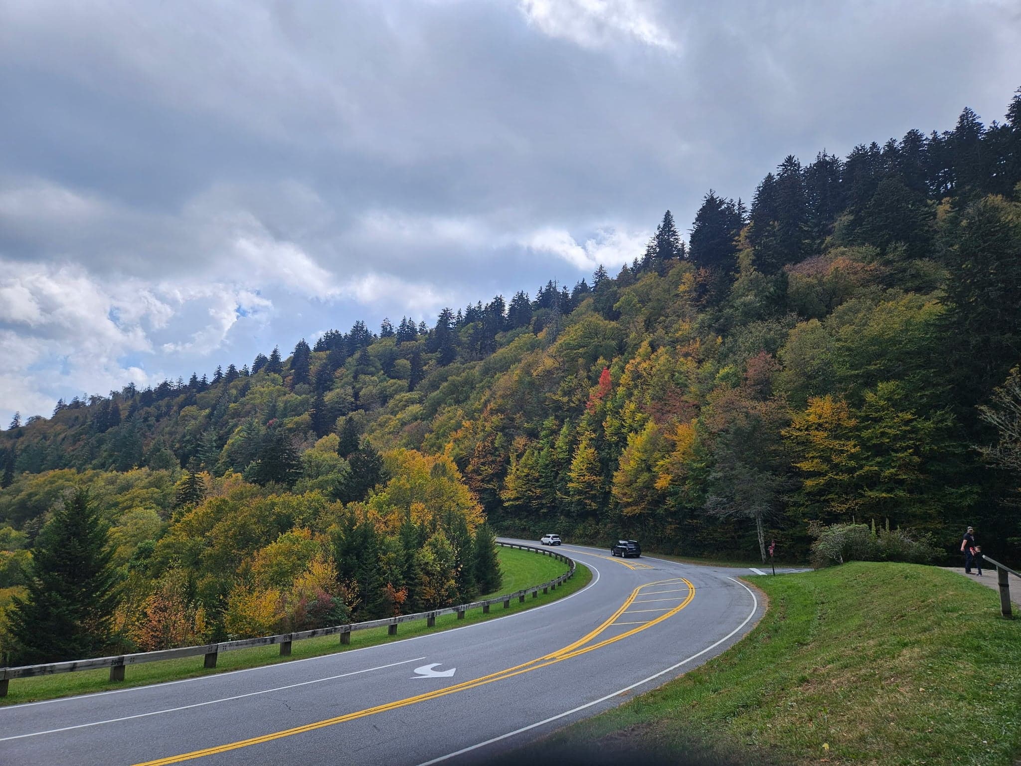A winding road curves through a vibrant forest of autumn-colored trees under a partly cloudy sky. A winding road curves through a vibrant forest of autumn-colored trees under a partly cloudy sky.