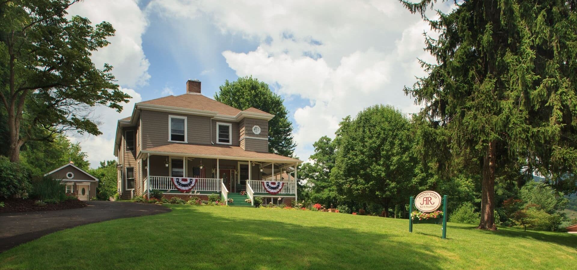 A charming two-story house with a porch, surrounded by green grass and trees under a cloudy sky.