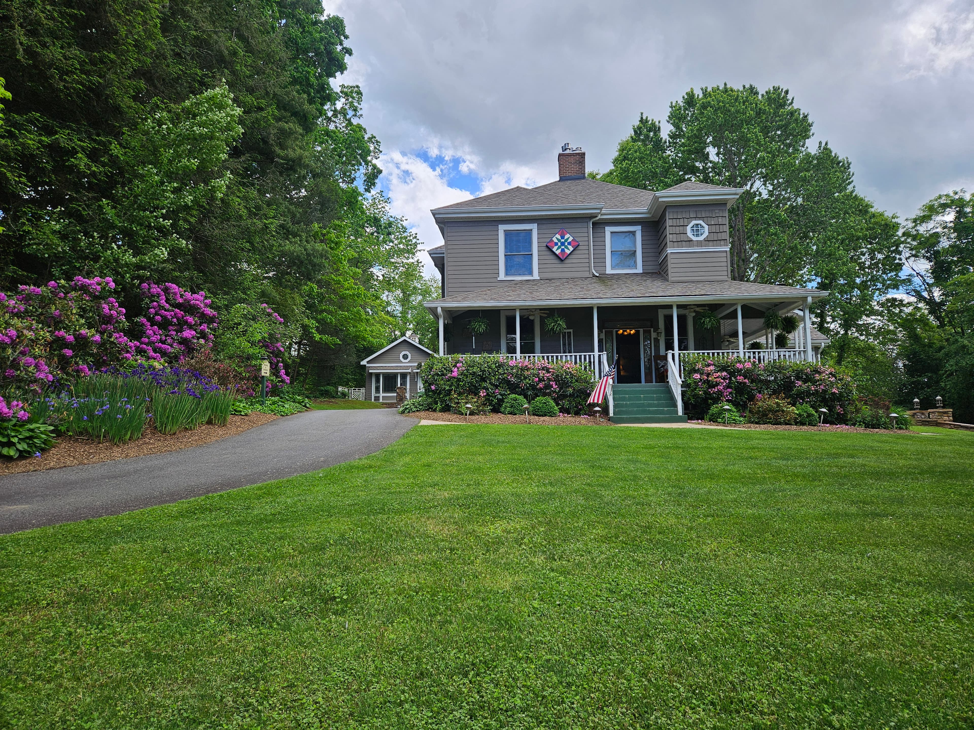 a house with a porch and a driveway with flowers in the spring