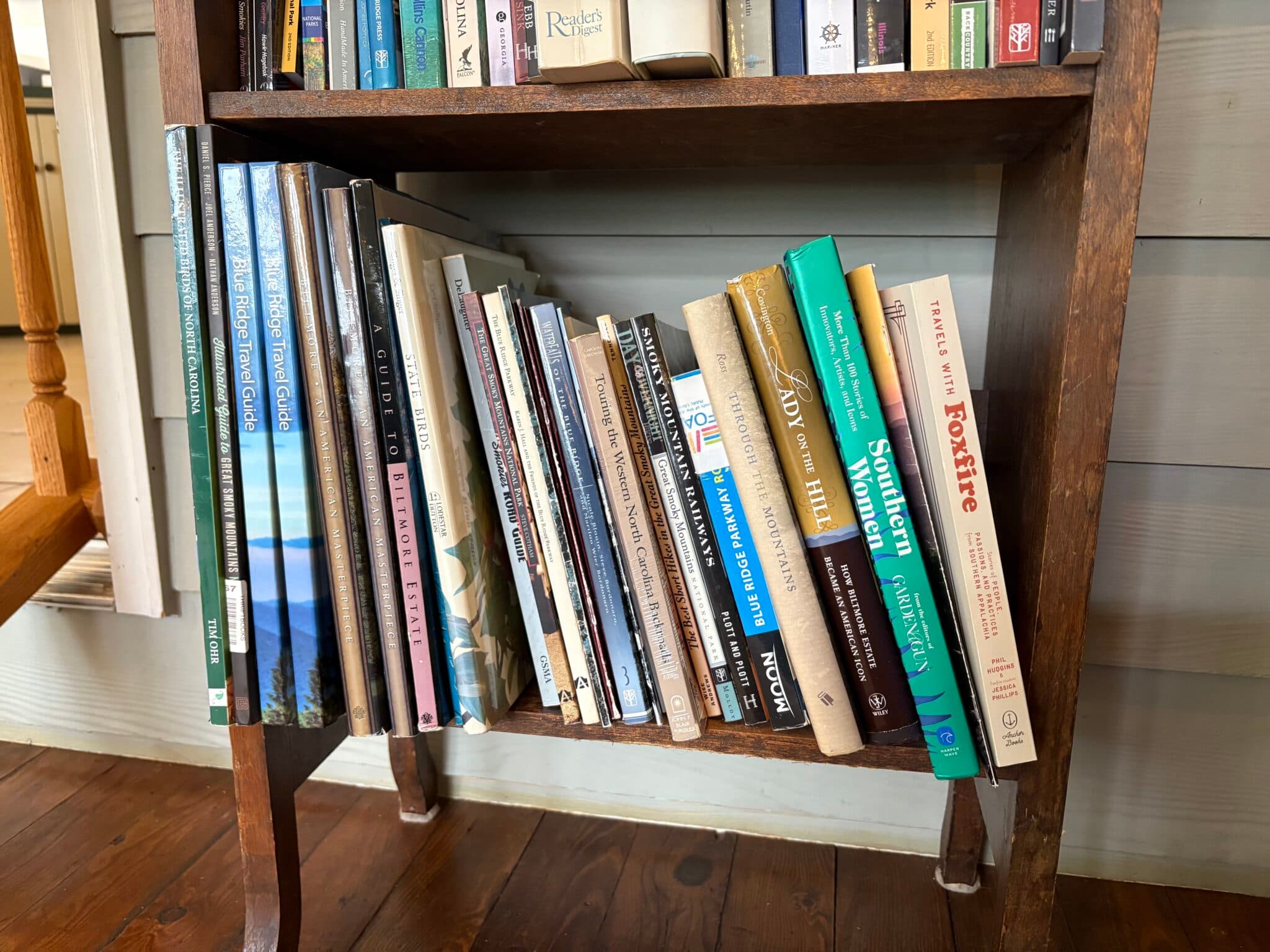 A wooden bookshelf displays a variety of stacked books. A wooden bookshelf displays a variety of stacked books.