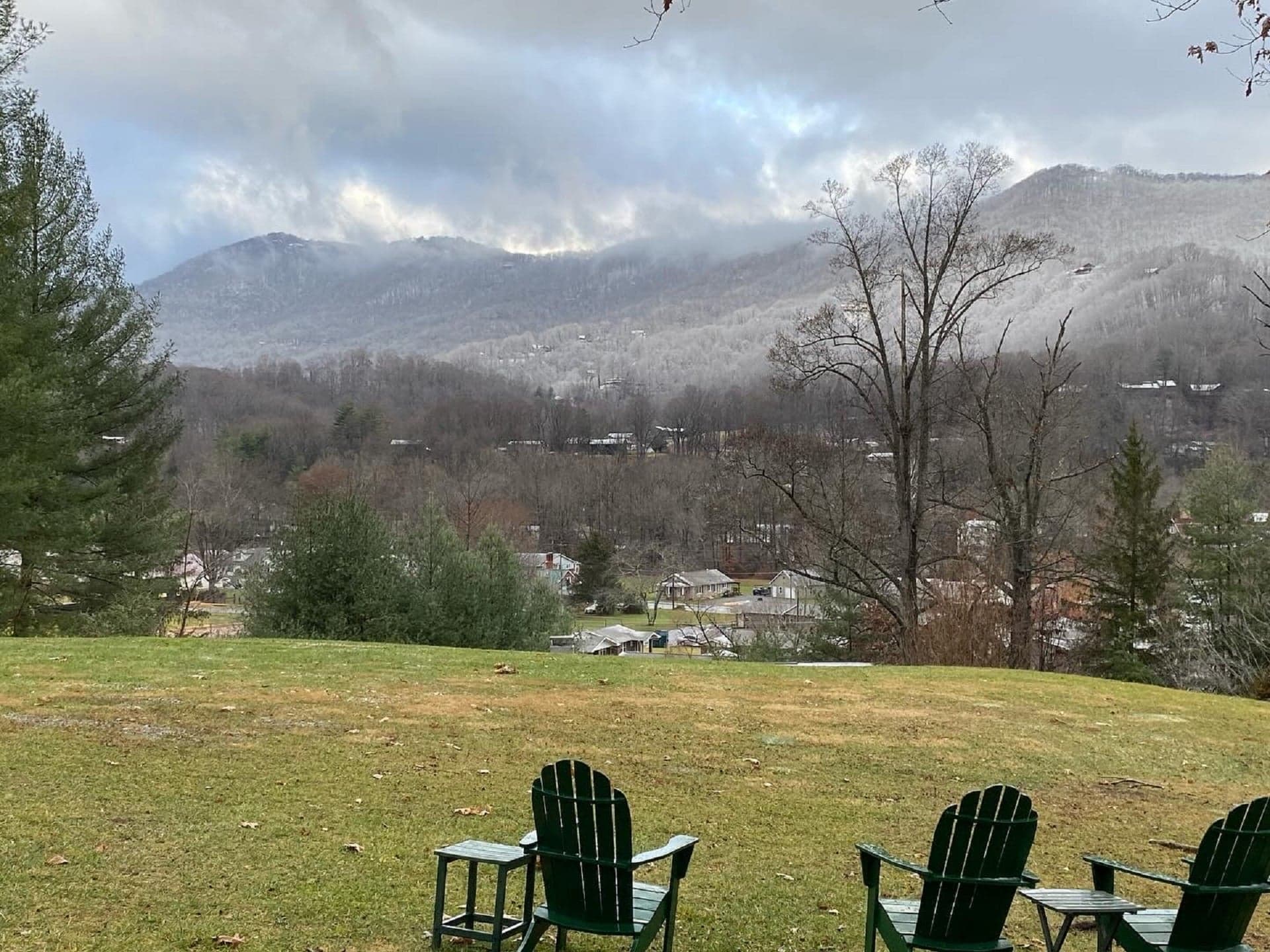 A serene view of misty mountains and a small town, with green chairs in the foreground.