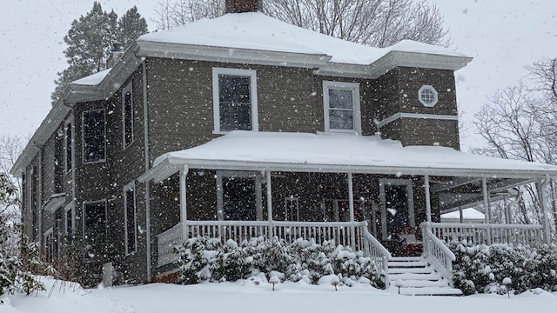 A large gray house is covered in snow while snowflakes fall steadily around it.