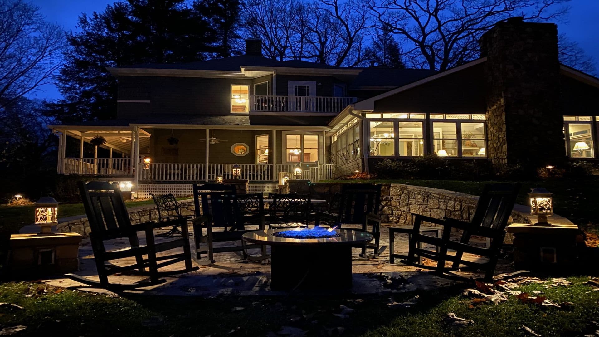 A cozy outdoor seating area with a fire pit, surrounded by a house, illuminated at night.