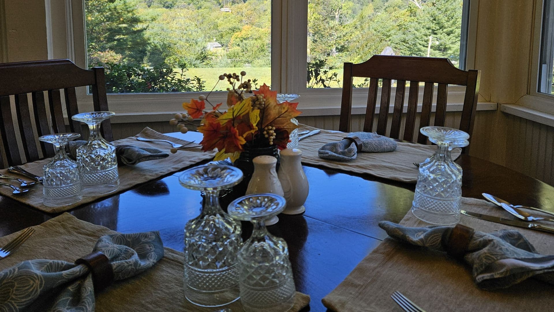 A dining table set with crystal glassware, decorative napkins, and a floral centerpiece, overlooking a scenic view.