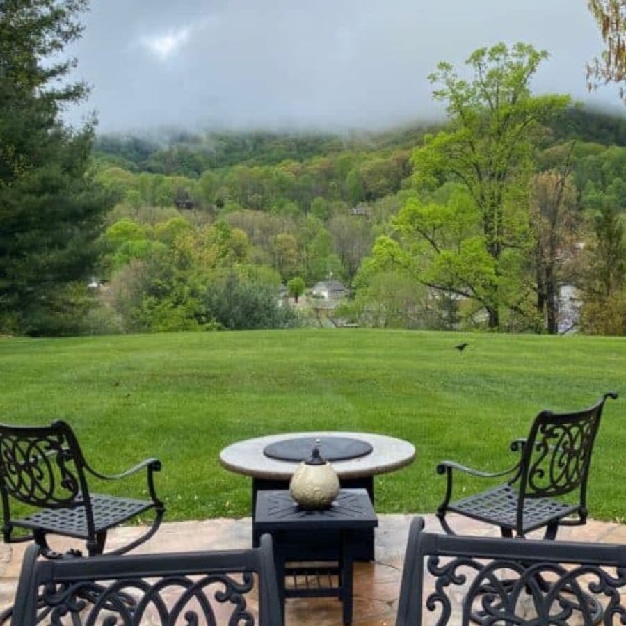 A serene outdoor view featuring two wrought-iron chairs and a coffee table overlooking a lush green landscape and misty mountains.